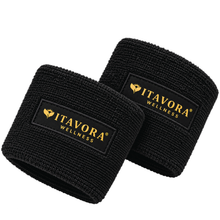 Vitavora Wellness Power Circle Wristbands shown as a pair, black terry cloth construction with woven gold logo patch, on a white studio background.